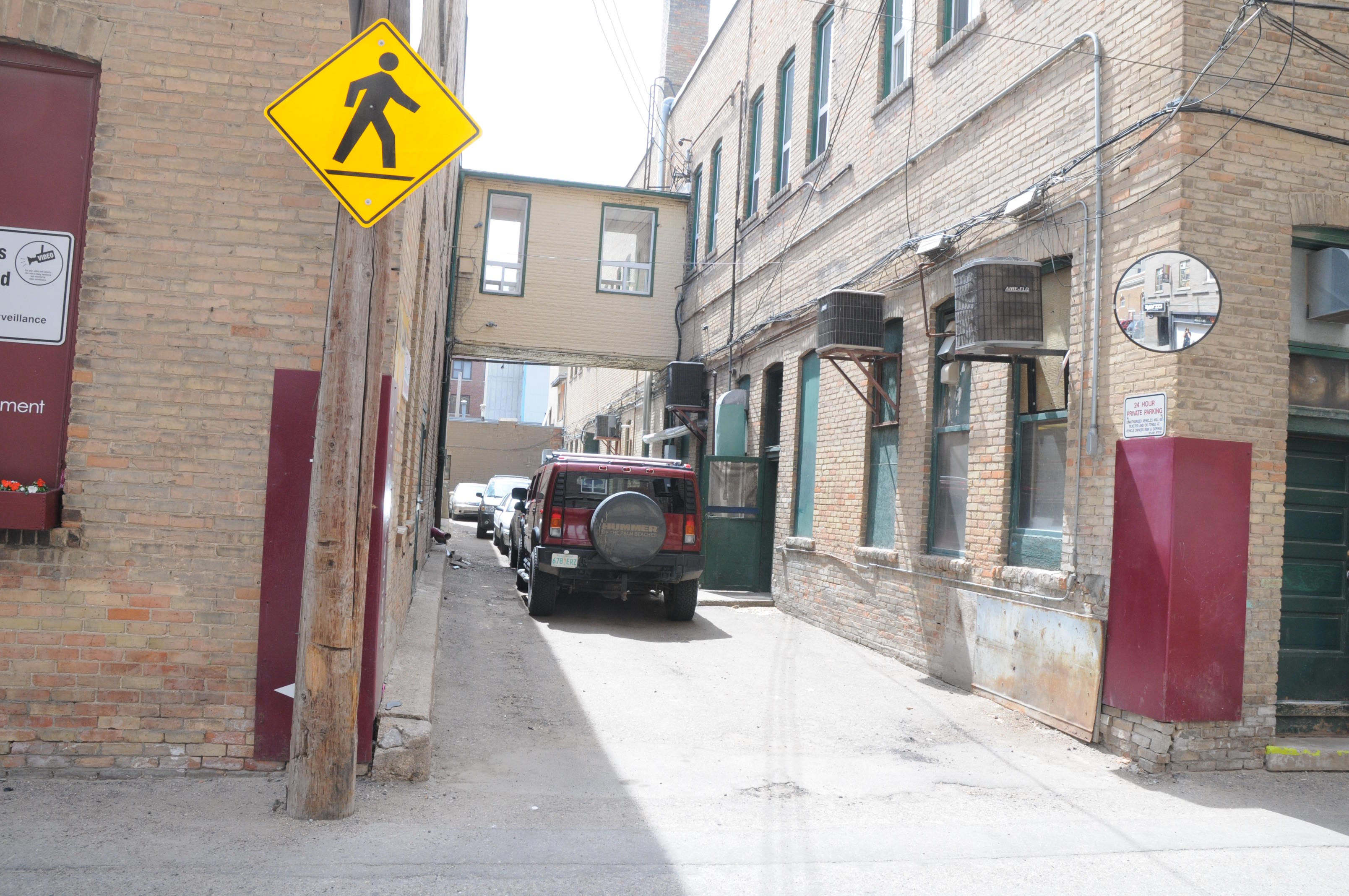 Outside image of the Traveler's Block alleyway overlooking the second story catwalk, with red Hummer parked in the alley.